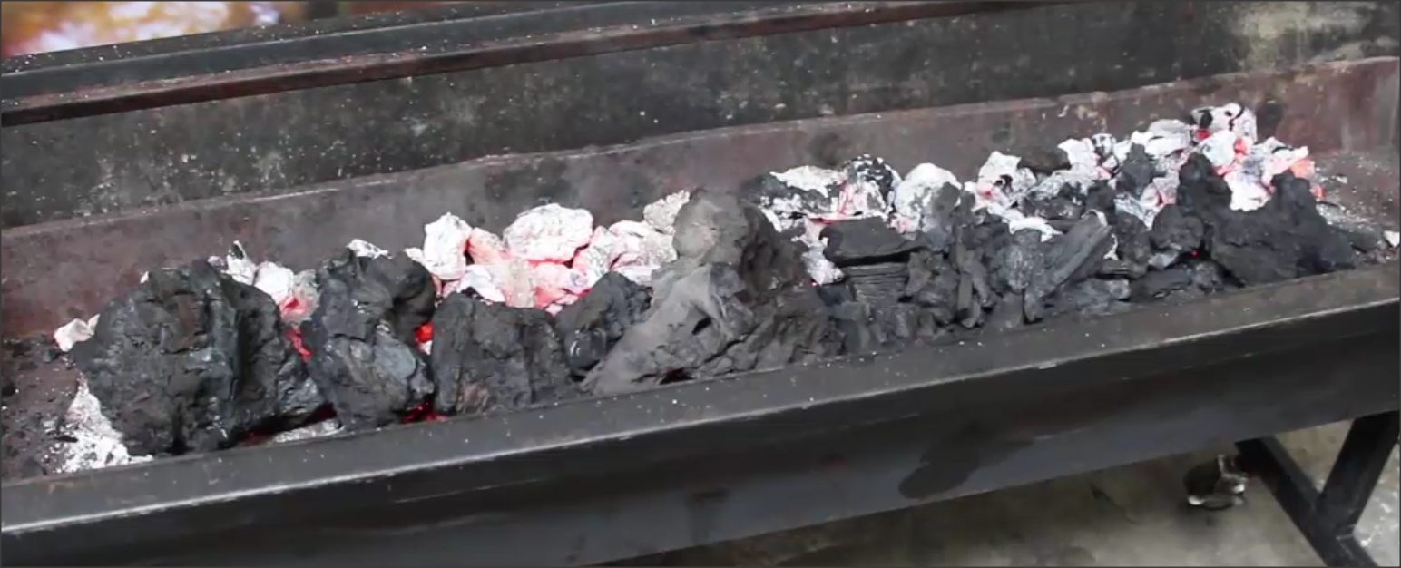 This image show how charcoal is added to a spit roaster during a cook